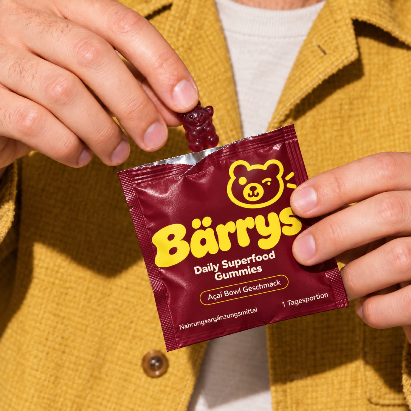 Hände öffnen ein Bärrys Päckchen, ein Gummibär schaut heraus