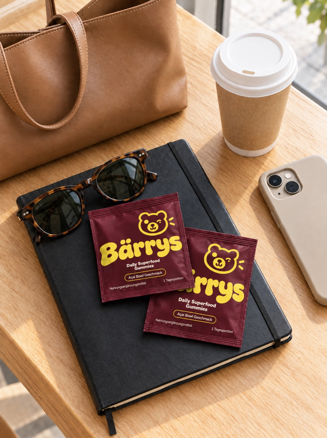 Zwei Bärrys Päckchen auf einem Notizbuch neben Kaffeebecher und Handtasche